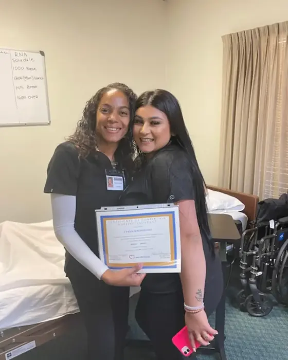 A graduate holding her nursing assistant certificate of completion beside instructor Tynesha Zacarias